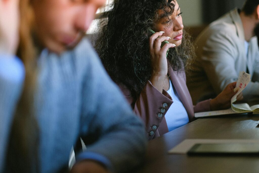 Focused businesswoman multitasking during a meeting, speaking on the phone and taking notes.